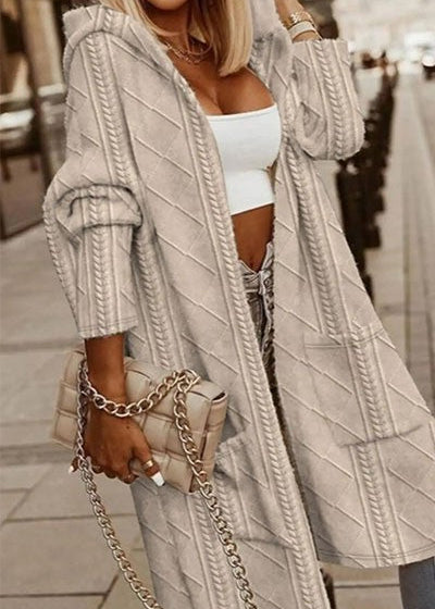 Woman wearing a long, light beige cable knit cardigan with a blurred background