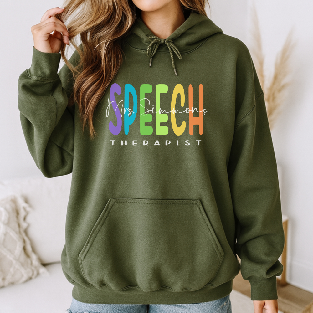 Person wearing a green hoodie with colorful text 'SPEECH THERAPIST' and 'Mrs. Simmons'.